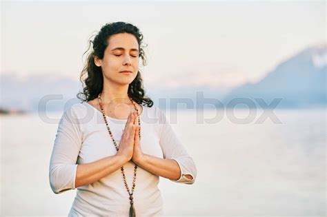 Beautiful Spiritual Woman Meditating By The Lake Wearing White Clothes