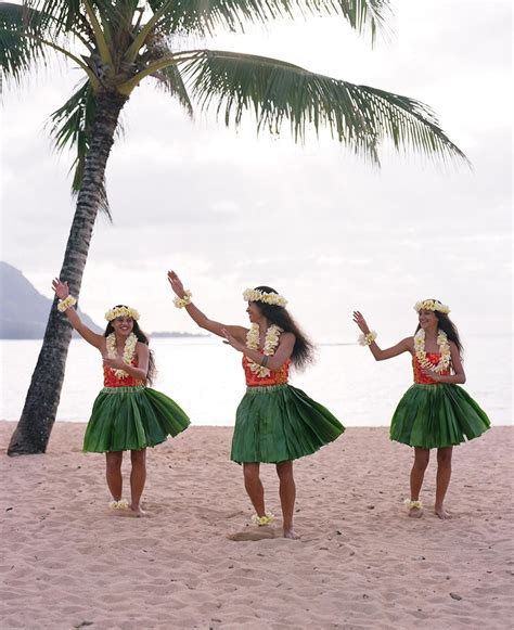 three women in green hula skirts dancing on the beach with palm trees