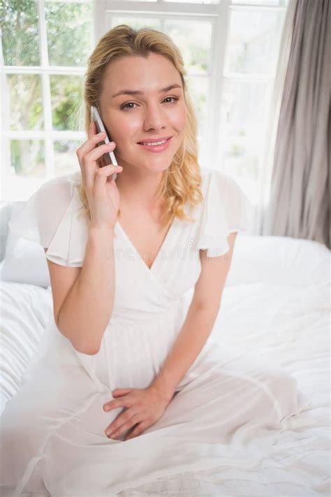 Pretty Blonde Sitting On Bed On The Phone Smiling At Camera Stock Image