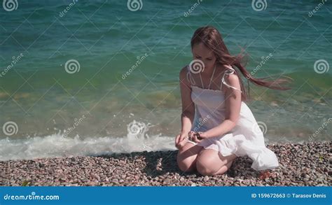 A Girl In A White Beach Dress Sits On A Rocky Seashore A Beautiful