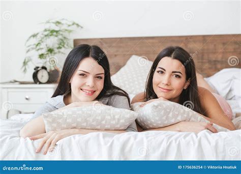 lesbian couple in bedroom at home lying hugging pillows smiling relaxed