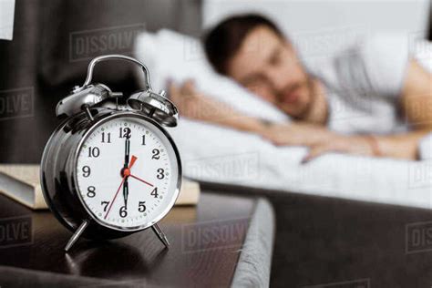 Close Up View Of Alarm Clock And Young Man Sleeping Behind Stock