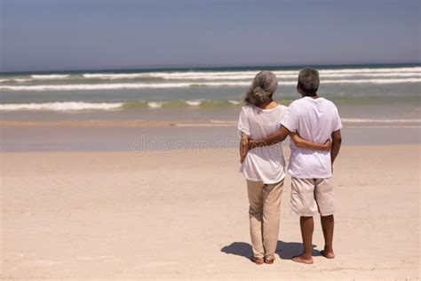 Senior Couple Standing On A Beach With Their Arms Around Each Other