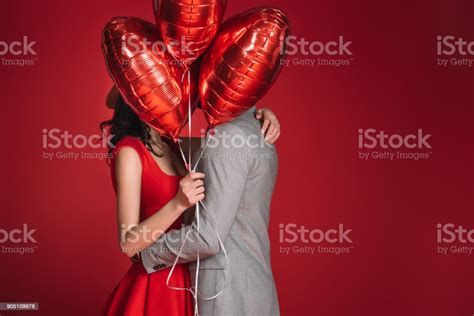 Couple Covering Faces With Bundle Of Balloons Isolated On Red Stock
