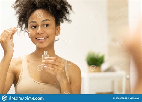 Attractive Woman Applying Serum On Face Moisturizing Skin Standing