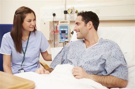 Nurse Sitting By Male Patient S Bed In Hospital Stock