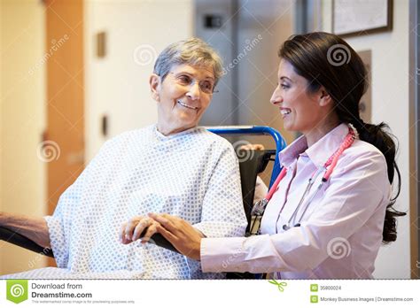 Senior Female Patient Being Pushed In Wheelchair By Doctor