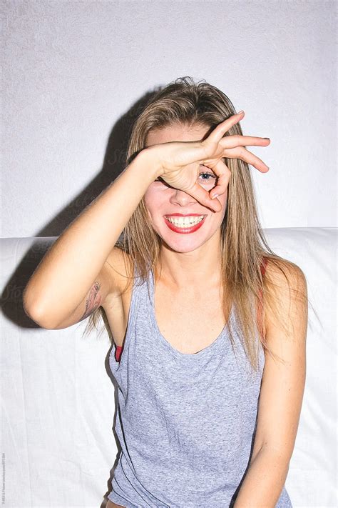 Smiling Young Woman Looking At Camera Through Hole Made By Fingers By