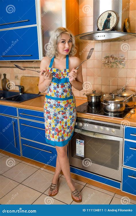 attractive naked blond housewife in an apron alone in a home kitchen