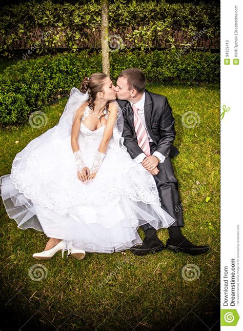 married couple sitting on lawn under tree and kissing