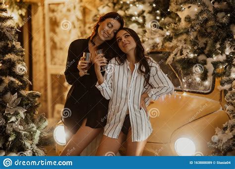 Lesbian Couple Holds Glasses Of Wine Against Background Of Christmas