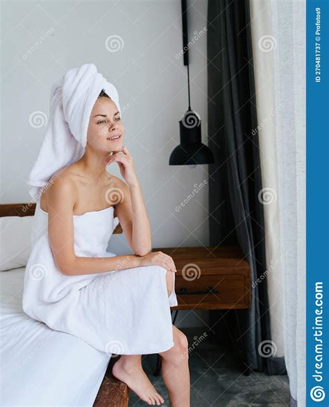 A Woman Sits On A Bed After A Shower With Wet Hair With A Towel On Head