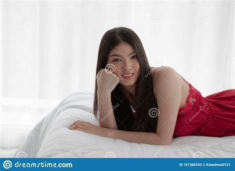 asian woman wearing a red dress lying on a white bed in a