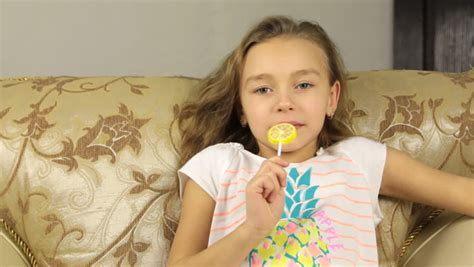 Girl Licking Candy On A Stick In The Form Of Lemon And And Smiling