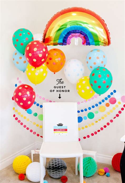 A Room Filled With Balloons And A White Chair In Front Of A Rainbow