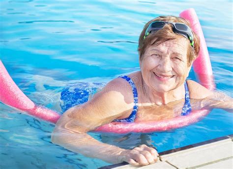Senior Woman Over Age Of 50 Doing Aqua Fitness With Swim Noodles In