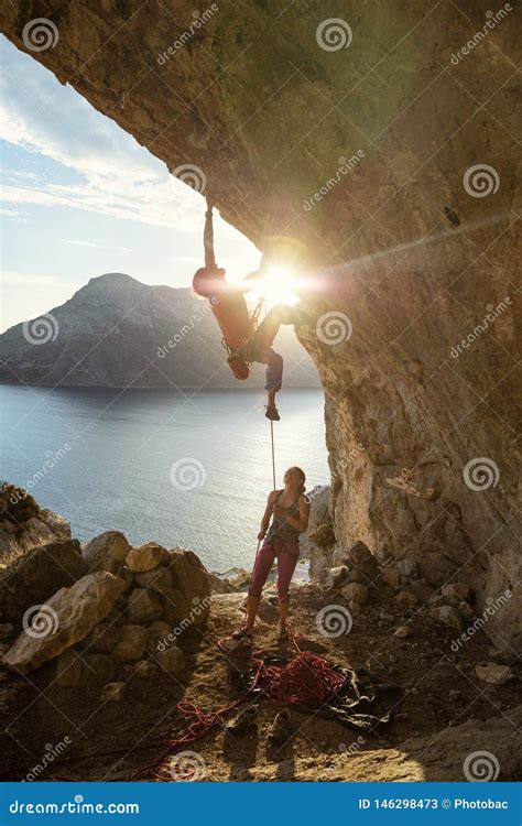 Male Rock Climber Starting Challenging Route On Cliff At Sunset Female