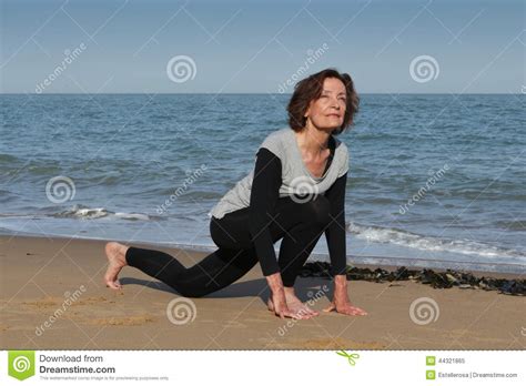 senior woman doing yoga sun salutation on the beach stock