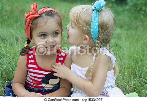 two girls sharing secrets among grass canstock