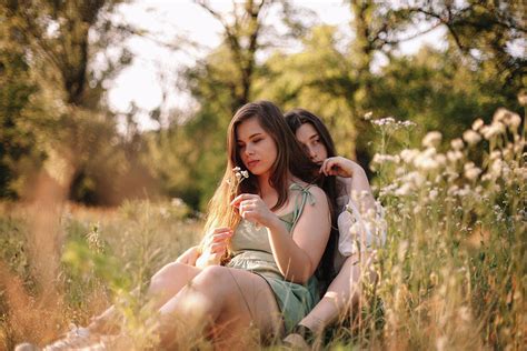Thoughtful Lesbian Couple Sitting In Field Of Flowers In Forest