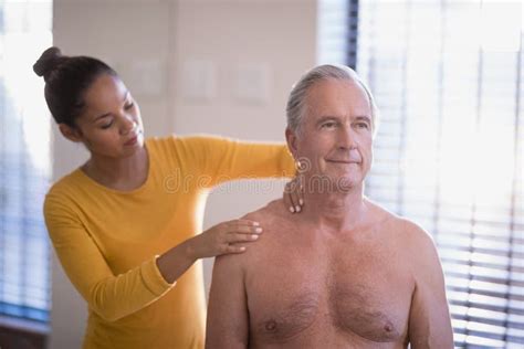 Shirtless Senior Male Patient With Arms Raised Receiving Neck Massage