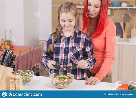 mother helping her daughter to mix salad ingredients