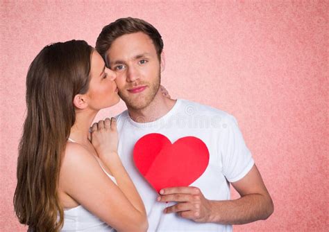 Romantic Woman Kissing On The Cheek Of Man Holding A Heart Shape Stock