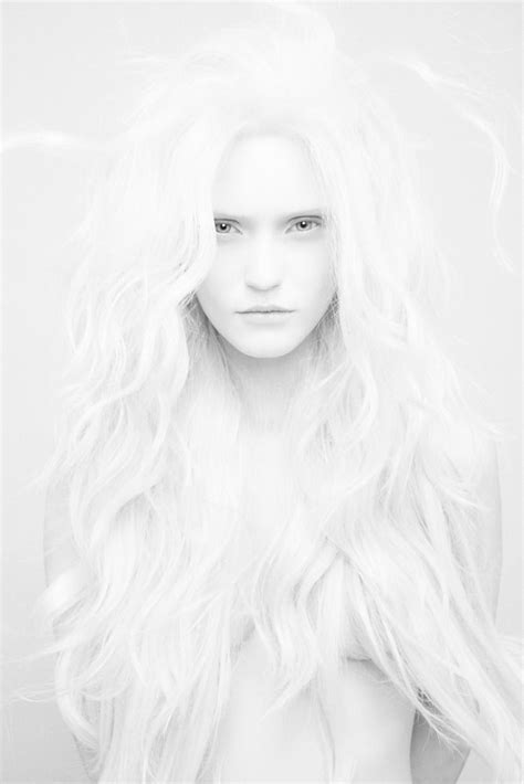 A Woman With Long White Hair Standing In Front Of A Gray Background And