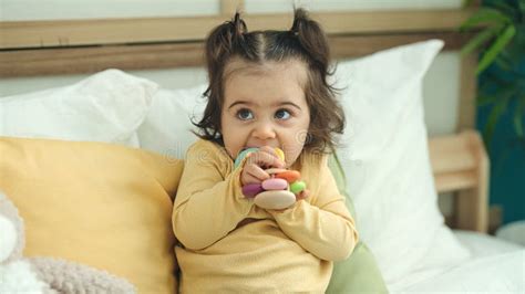 Adorable Hispanic Girl Sucking Toy Sitting On Bed At Bedroom Stock