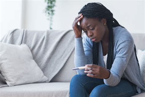 depressed black girl holding pregnancy test upset with positive result