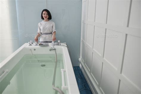 smiling assistant prepares hydro massage bath full of clear water in