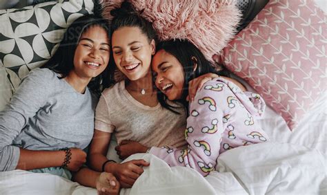 three teenage girls laughing and having fun while lying on bed together