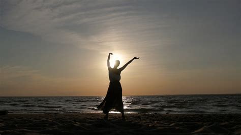 silhouette of a woman at sunset dancing on the beach flying skirt