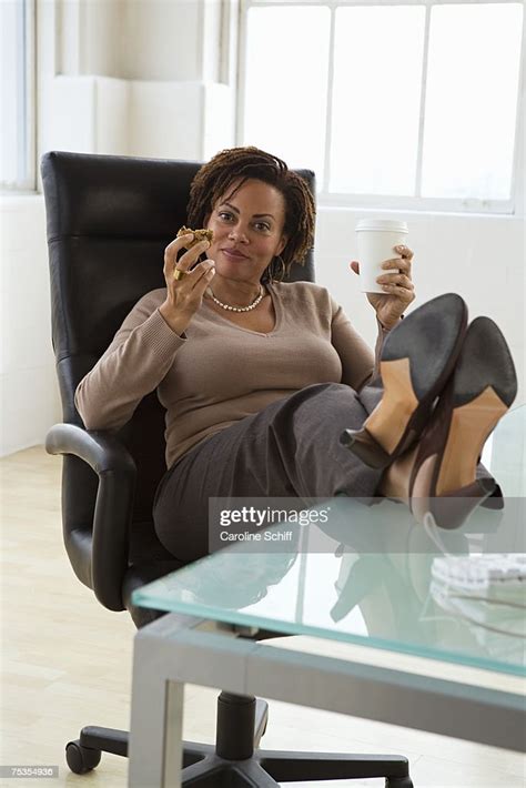 mature businesswoman having snack sitting with feet on desk portrait