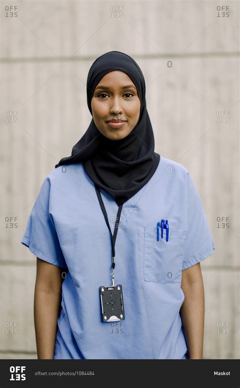 Portrait Of Smiling Female Nurse Wearing Hijab Against Wall In Hospital