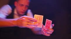 Close-up, Hands of a Magician Performing Tricks with a Deck of Cards. Neon Lighting and Smoke. Conjurer Shows Focus. Camera Quickly Rotates 360 Degrees.