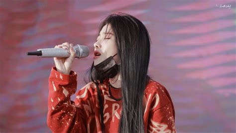 a woman with long black hair singing into a microphone