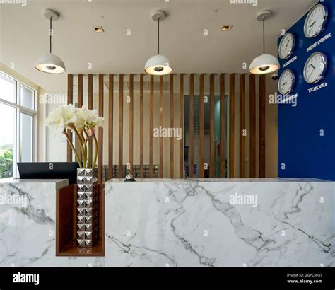 A long white marble reception counter located in the hotel lobby. The side wall has a clock to ...