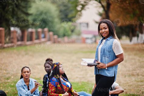 Group of five african college students spending time together on campus at university yard ...
