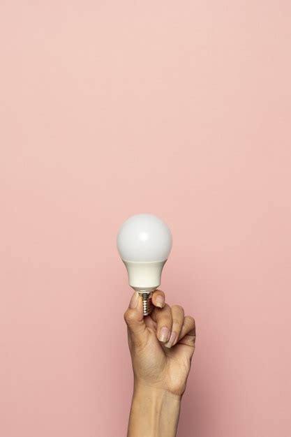 Vertical shot of a hand holding a light bulb isolated on a pink surface ...
