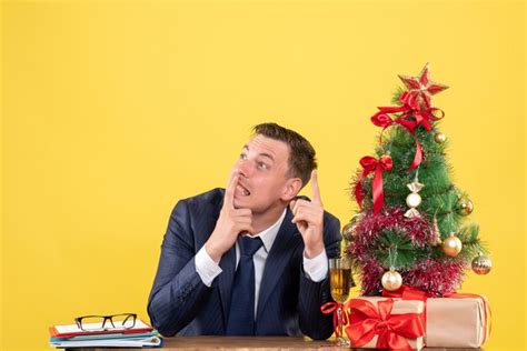 Front view of thinking man sitting at the table near xmas tree and ...