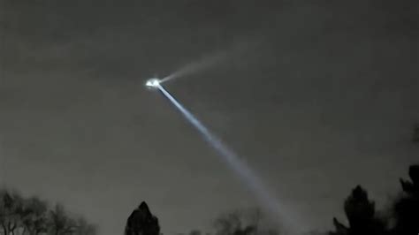 A bright spotlight beam shining from a flying object in the night sky ...
