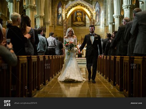 Bride and groom walk down church aisle holding hands stock photo - OFFSET