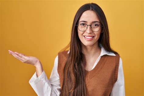 Junge brünette Frau steht vor gelbem Hintergrund und trägt eine Brille ...