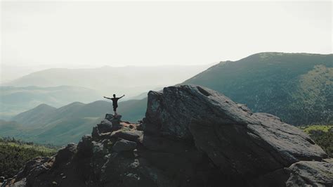 A man standing on top of a mountain with and raising his hands up the ...