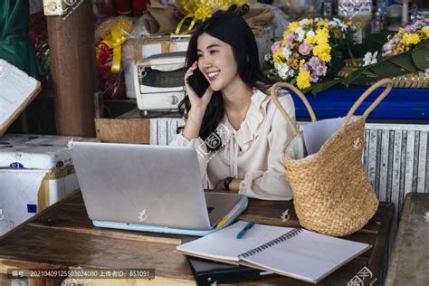 穿着休闲衬衫的泰国工作女商人在电话里谈笑风生。在家里用笔记本电脑工作。,摄影素材,汇图网www.huitu.com
