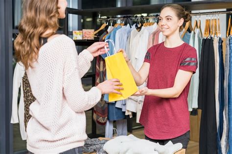 Female seller giving yellow shopping bag to woman | Premium Photo