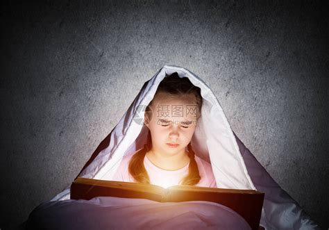 害怕的孩子带着打开的书和手电筒躲在毯子下害怕的女孩闭着眼睛躺在家里的床上孩子读童话穿着睡衣的女孩在墙壁高清图片下载-正版图片506232486-摄图网