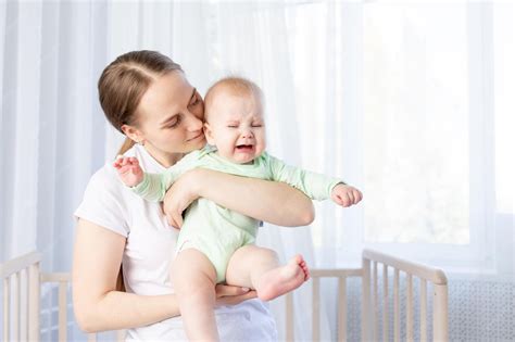 Premium Photo | Mom with a crying baby in her arms at the crib in the ...