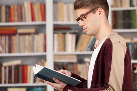 Reading his favorite book. Side View of young man reading a book while ...